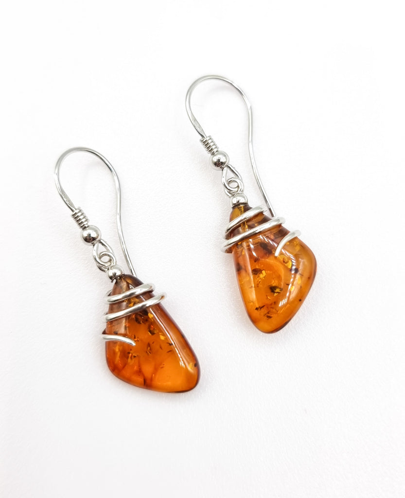 Exclusive earrings featuring abstract triangle shaped natural Baltic Amber gems intricately crafted with a swirl sterling silver encasing. The gorgeous warm cognac hues add a touch of sophistication to this  beautiful pair of earrings. Origin Poland