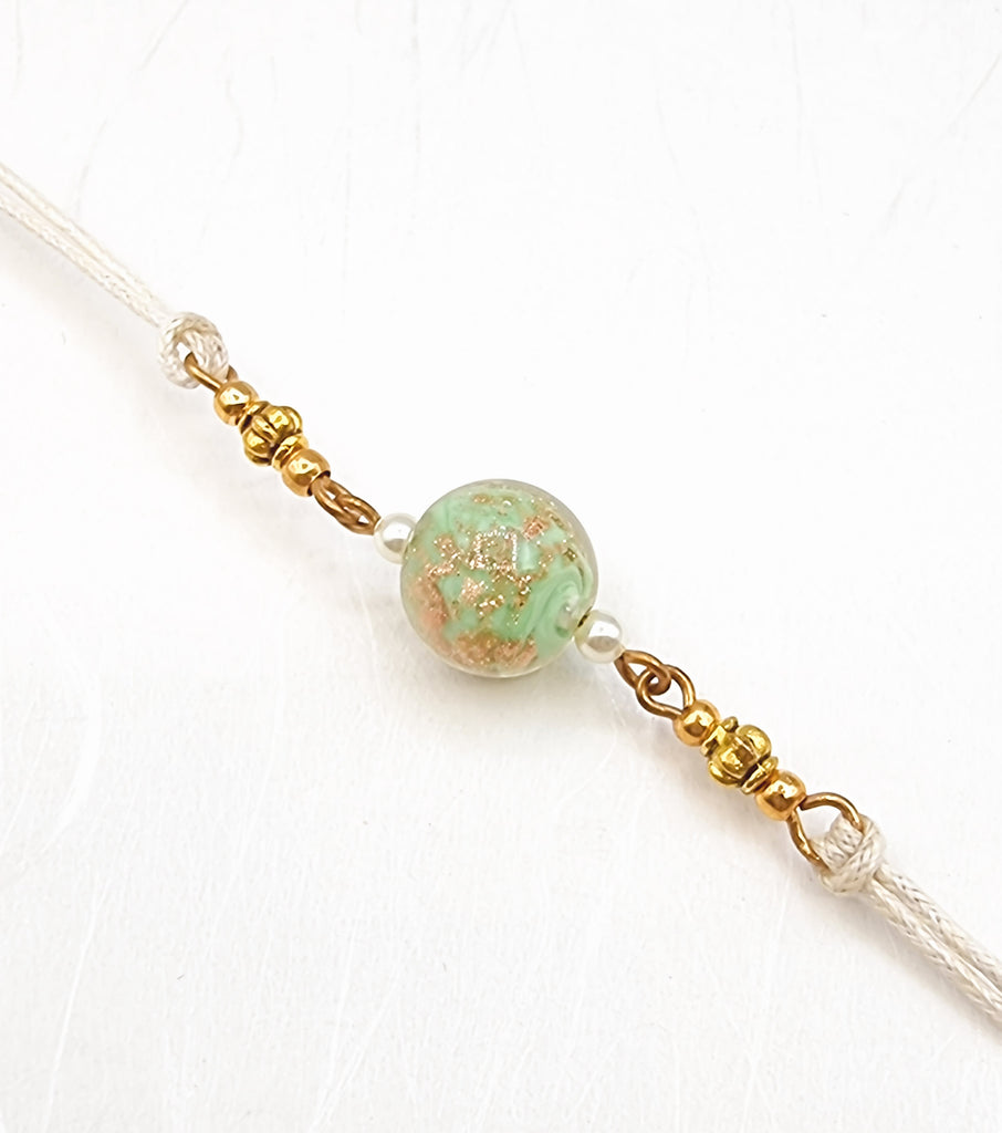 A handmade Rakhi delicately crafted with a gorgeous pastel green Handblown Glass with tiny specks of gold and accentuated with gold beads. Truly unique and one-of-a-kind!
