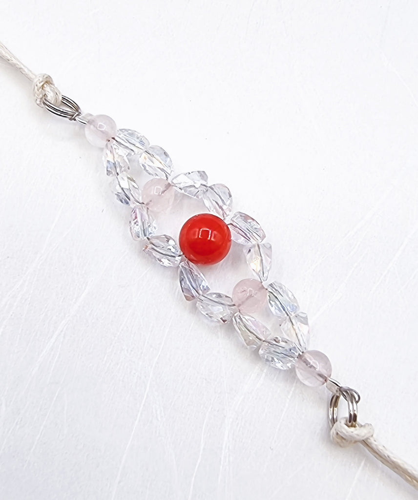 A handmade Rakhi delicately woven and crafted with sparkling crystals and natural Rose Quartz gemstone, with a synthetic red coral accent. Truly unique and one-of-a-kind!